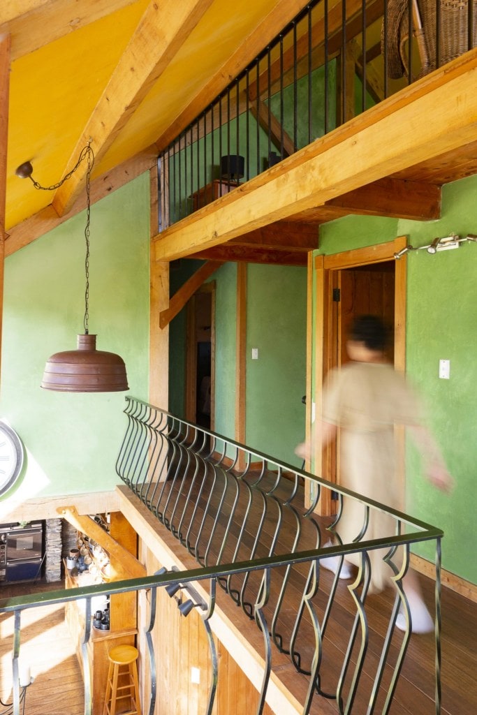 A woman walking through an upper level of a Welsh style cottage with limewashed green walls