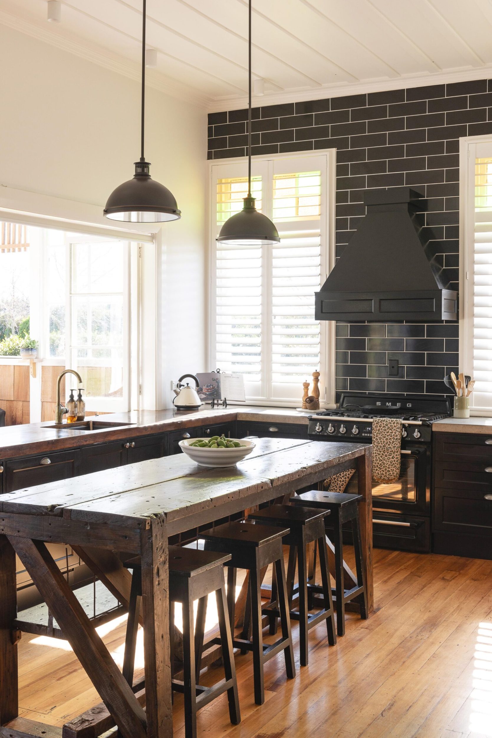 A kitchen with black subway tiles, polished wooden floors and a vintage dark wood island with stools