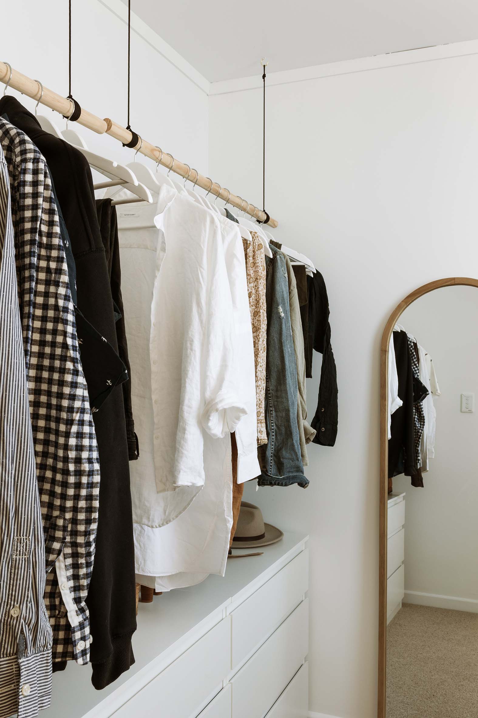 A walk in wardrobe with a large standing mirror and hanging hangers