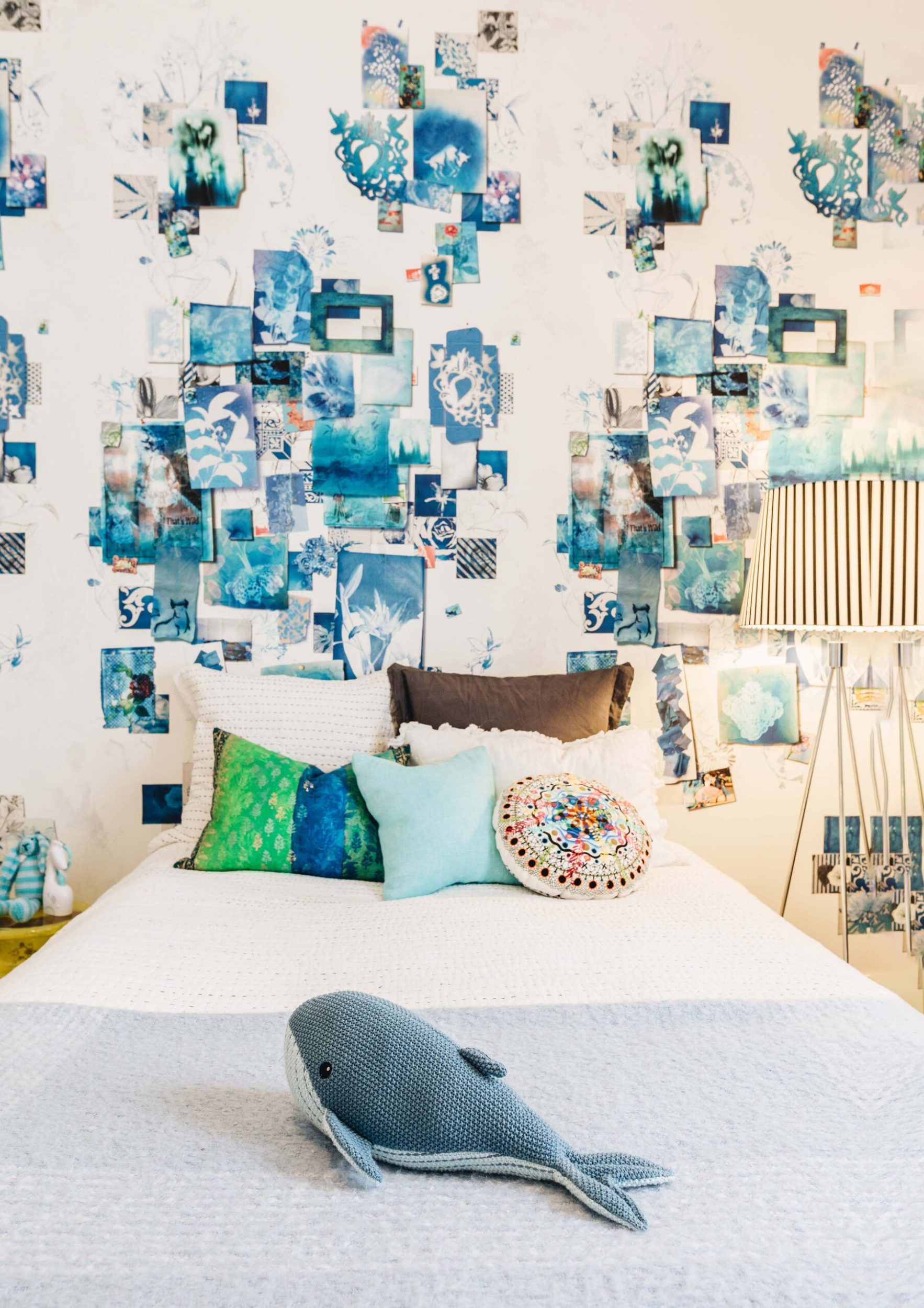 Bedroom with printed blue postcard wallpaper, a bed with light blue bedspread and soft toy whale sitting on top of it