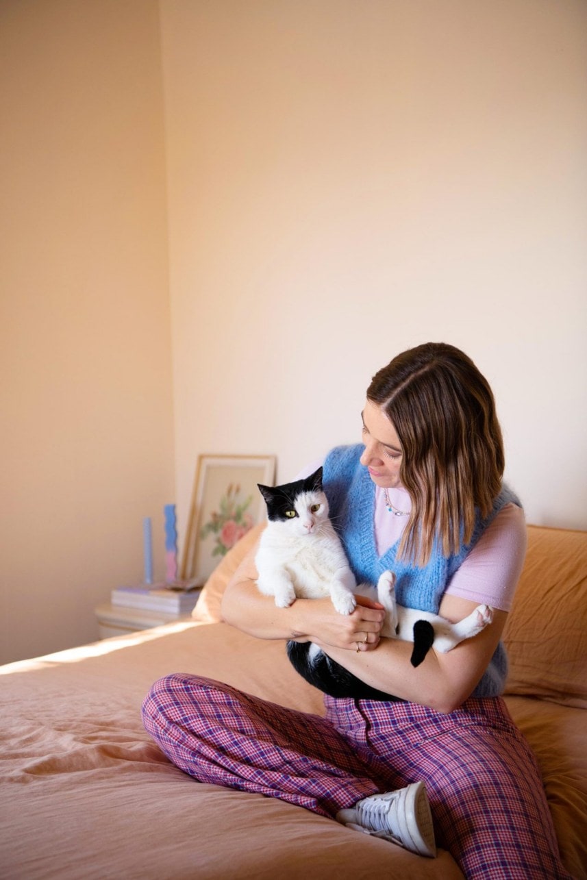 Danni Duncan sitting on a brown bed holding her black and white pet cat Stanley
