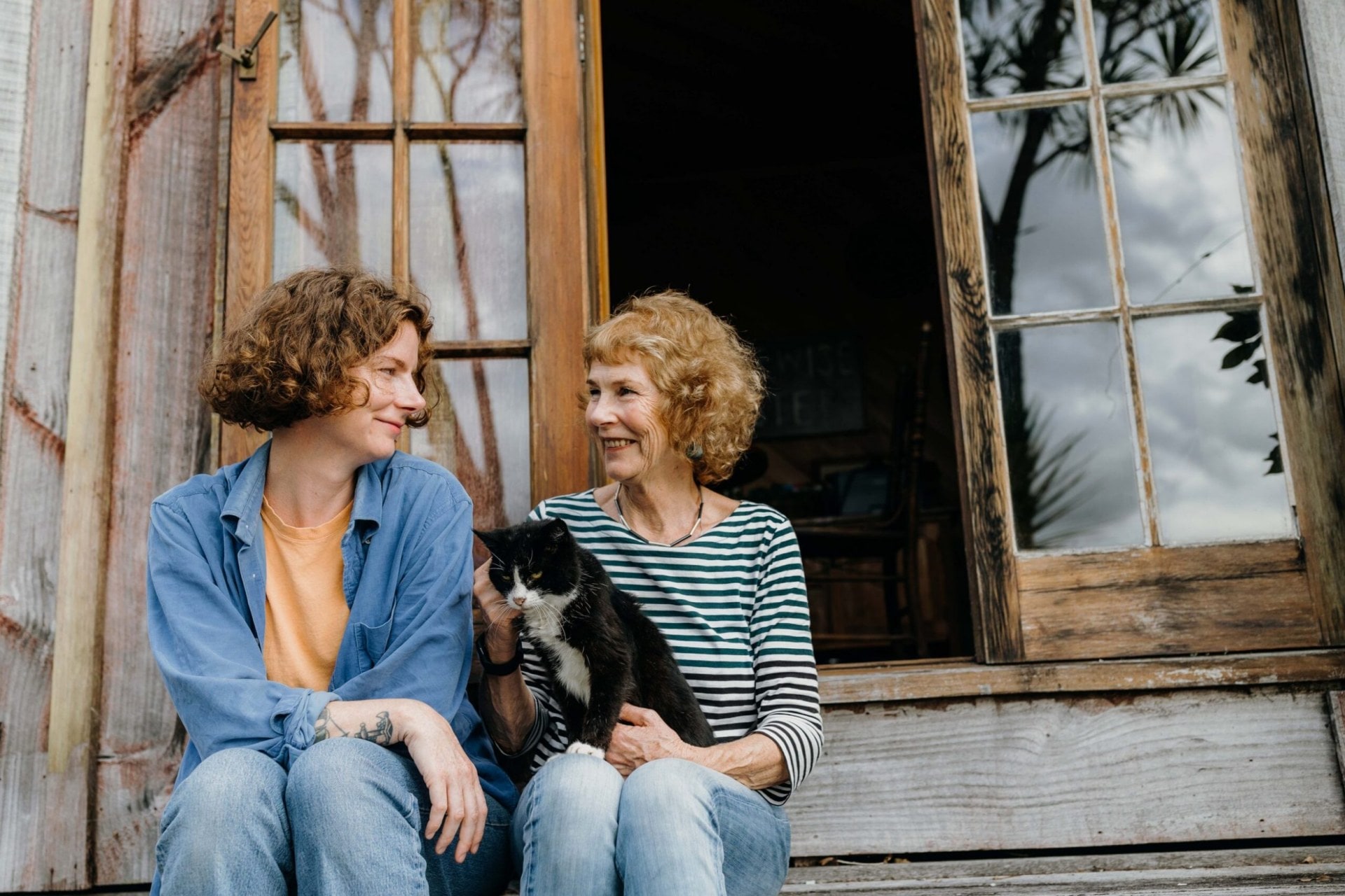 Kate Newby sitting on wooden steps with her mum Margaret and cat Wendy