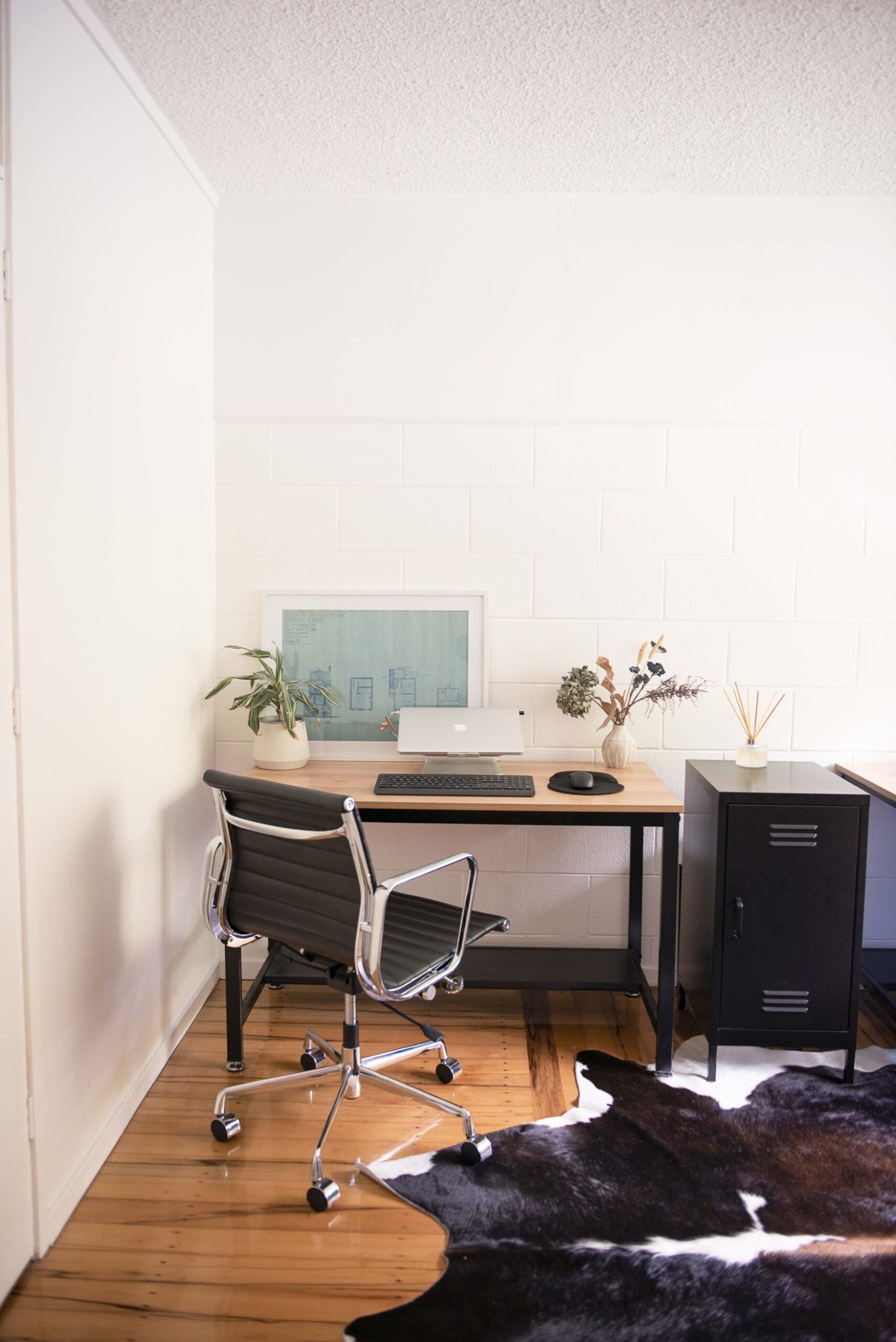 An office with polished wooden floors, a black chair, brown desk, black locker and cow hide rug