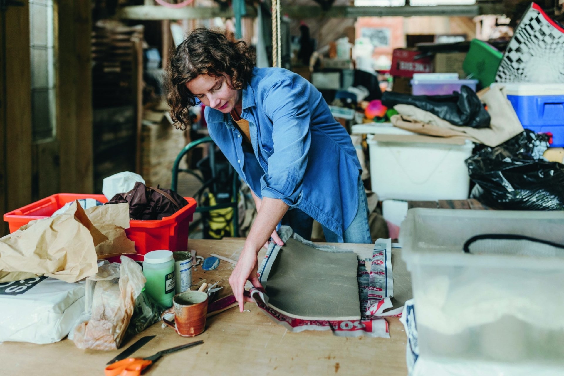 Kate Newby rolling a large piece of clay in her studio 