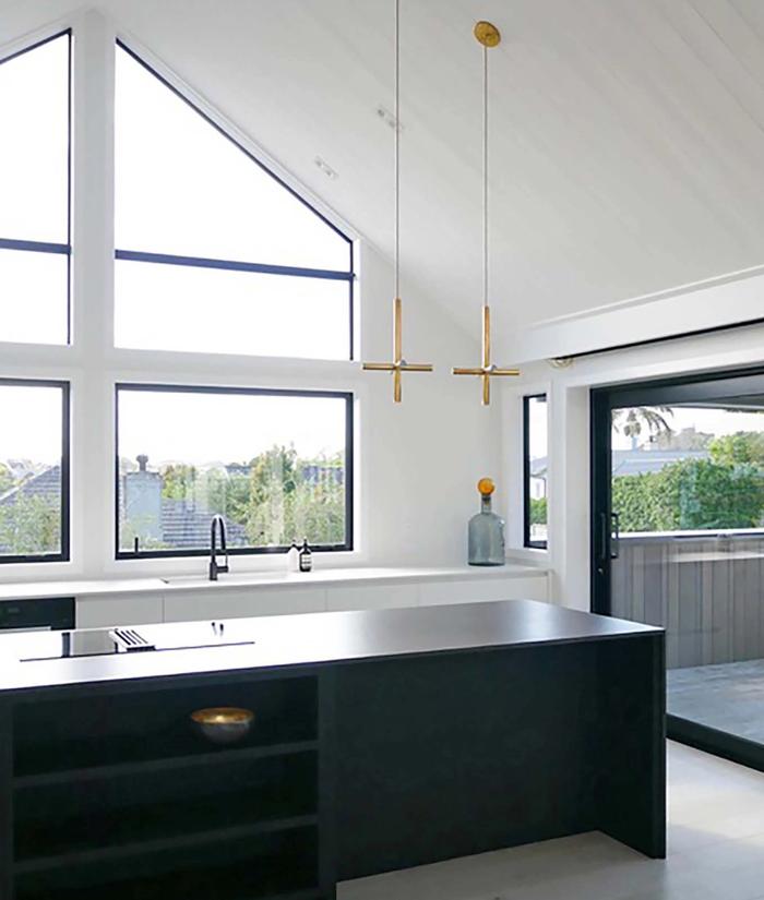 Black kitchen in a large room with cathedral ceilings and windows that match the pitch of the ceiling, two pendant lights hang above the island