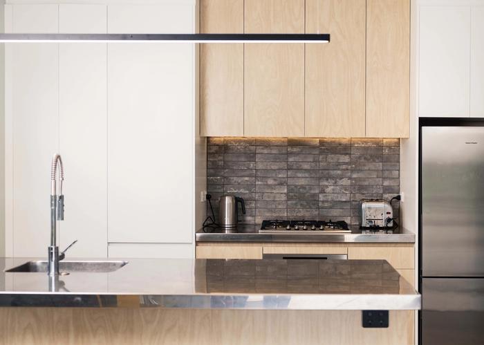 A white and timber kitchen with an thin, black architectural light fitting above the island