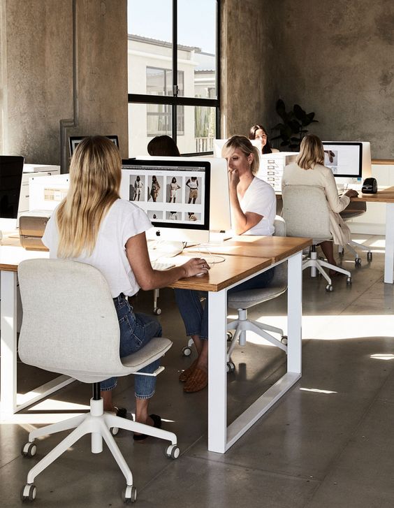 4 women in an office with concrete floor and walls. Sitting at computers.