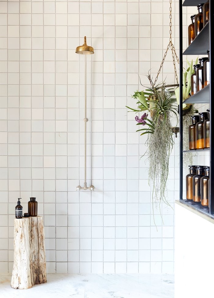 White tiled bathroom with gold shower head and black shelves