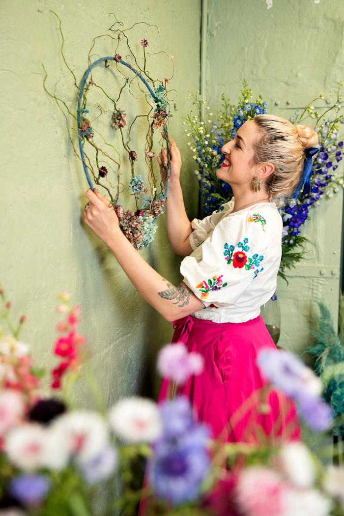 Dried floral wreath being hung on green wall by floral artist Georgie Malyon