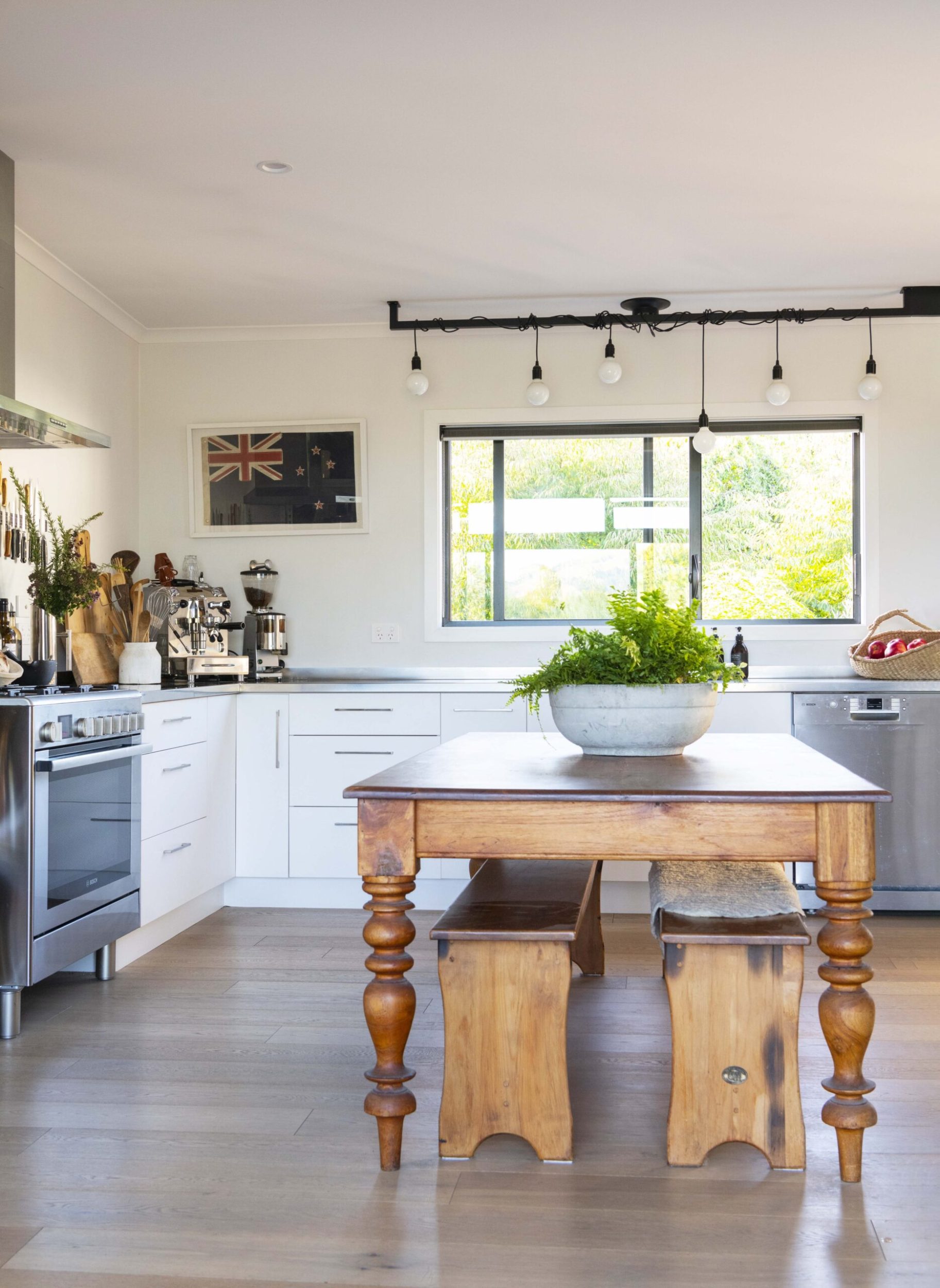 A kitchen with a large wooden table, white countertops and hanging lights