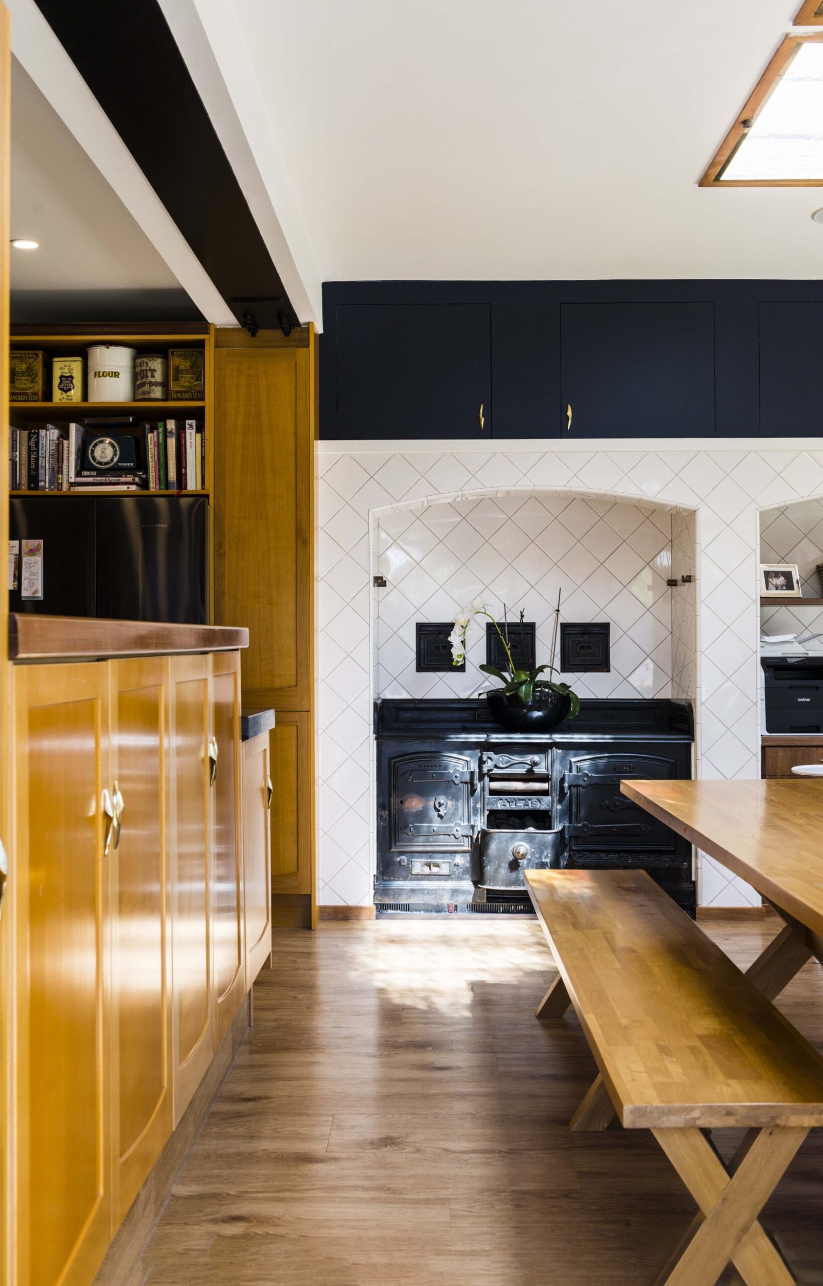 A white tiled kitchen with wooden flooring and a black vintage stove