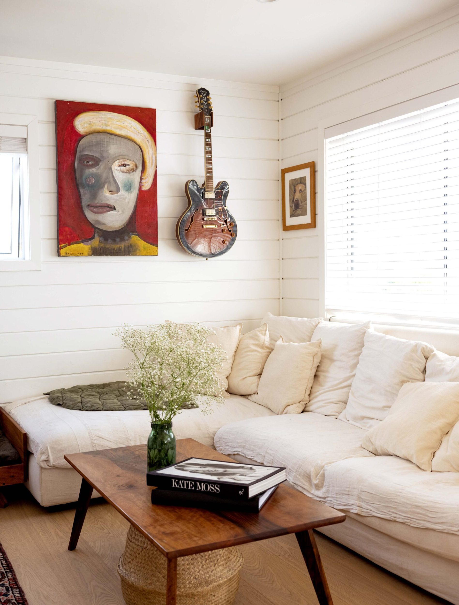 Corner of lounge with white linen couch and large painting and guitar on the wall