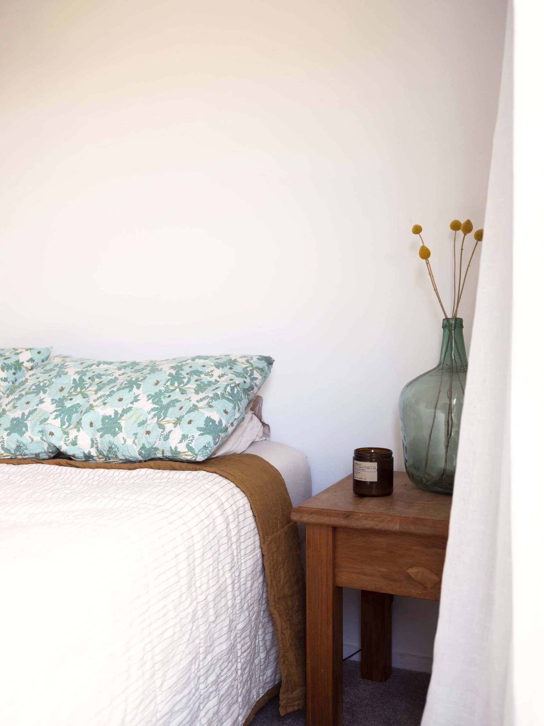 Bed with blue flower pattern pillows with large green glass bottle on bedside table