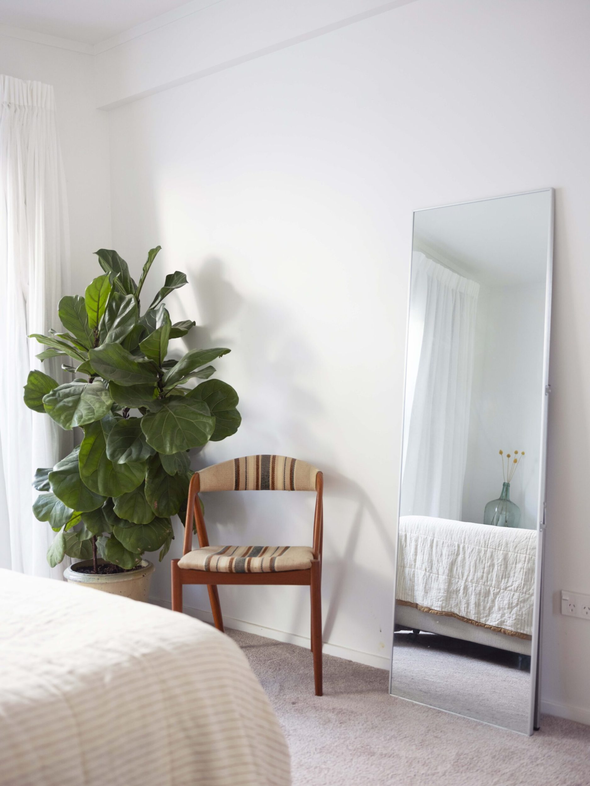 Corner of bedroom with full length mirror, fiddle leaf fig plant and chair