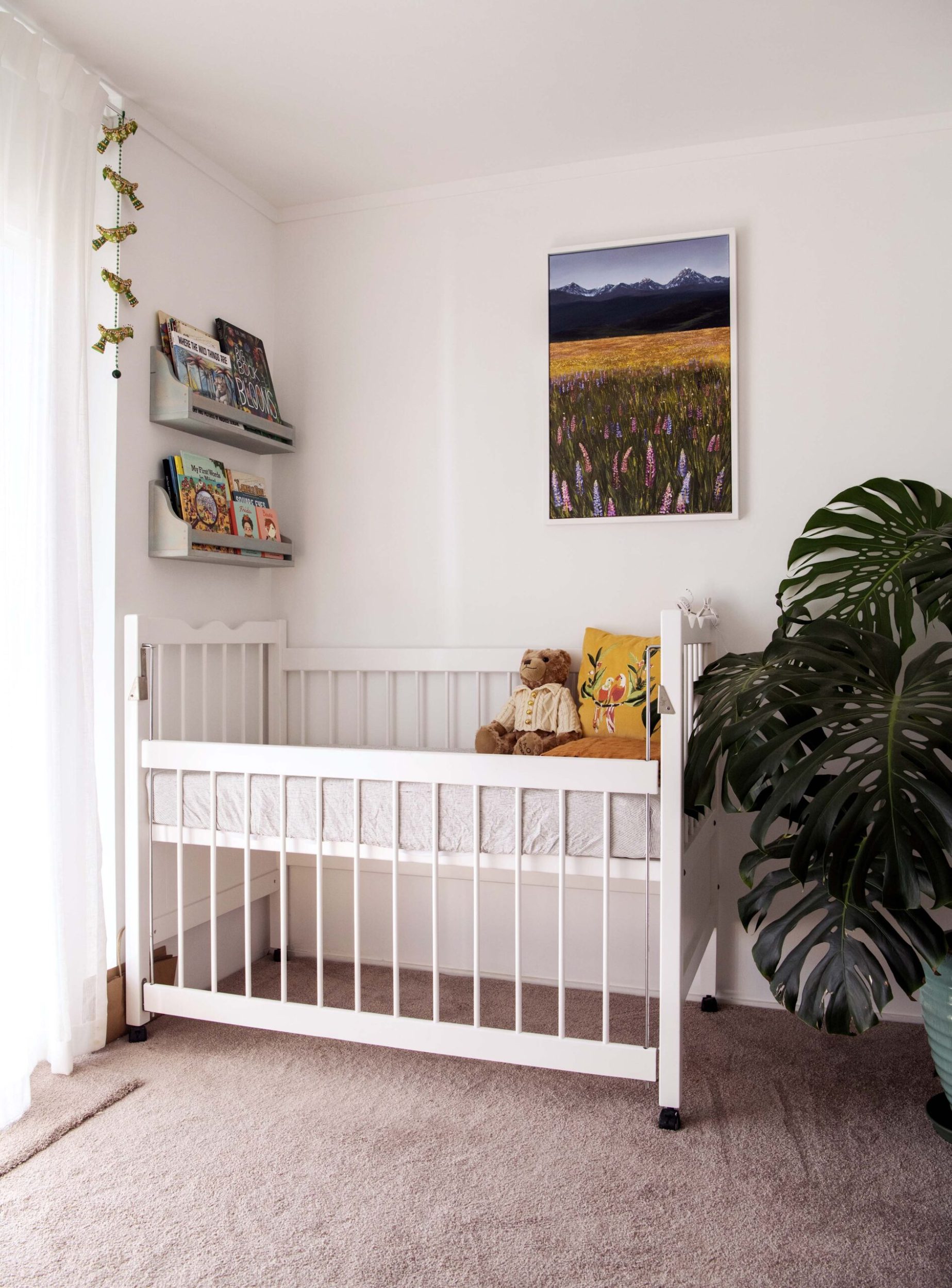 White cot with monstera plant to the right and book with shelves to the left