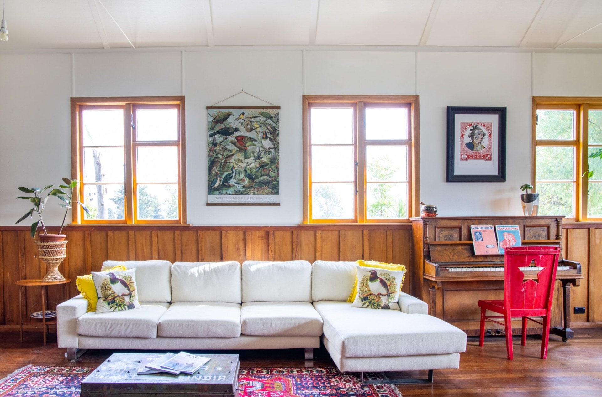 Living room with white walls and wood panels, a white couch, red patterned rug and assorted hanging artworks 