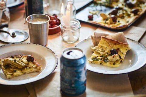 Slices of blanco pizza on rustic white plates on a dinner table with candles