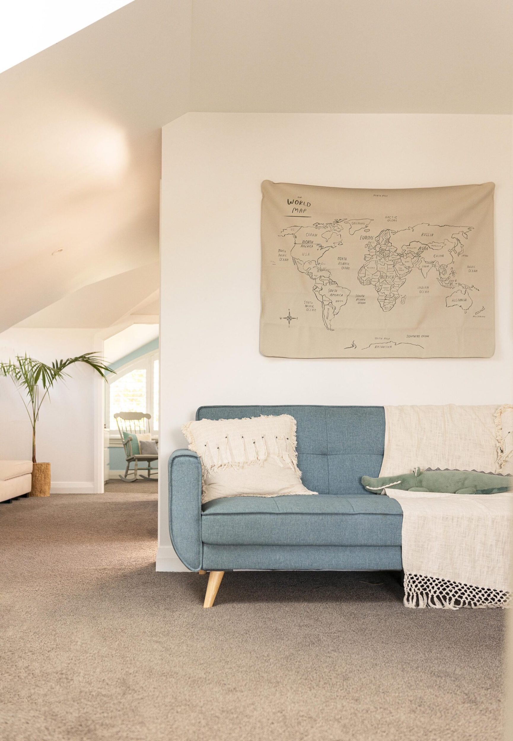 A blue couch pushed against a wall with a cloth hand drawn world map