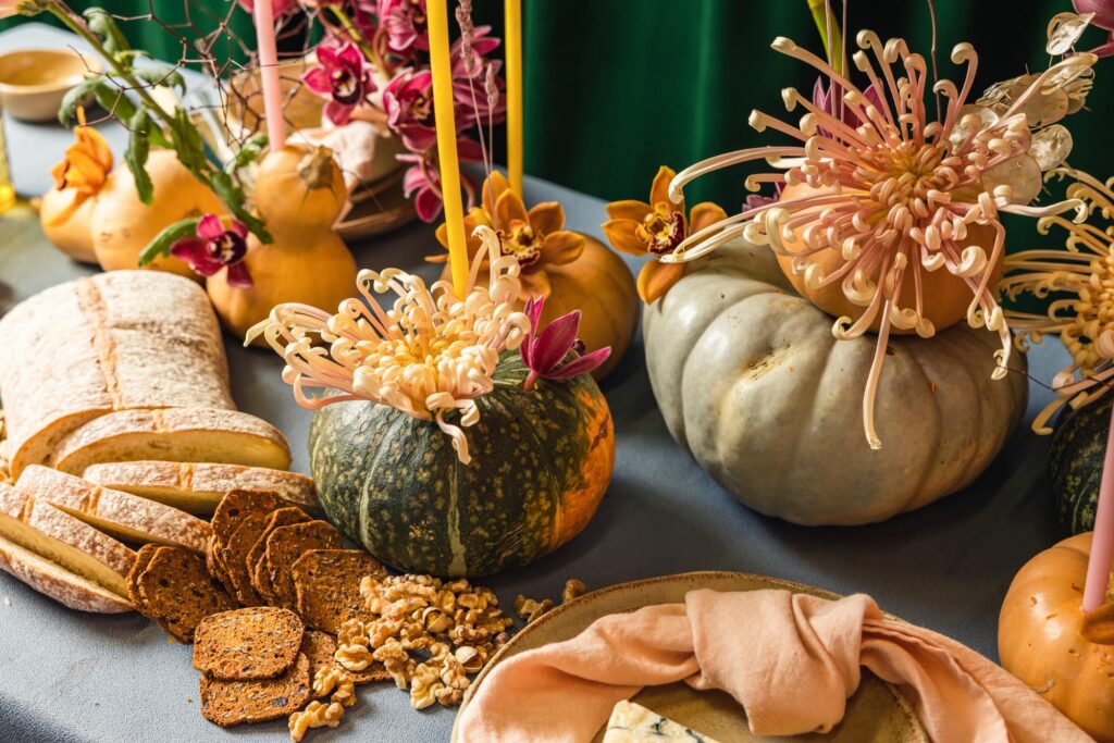 A table spread laden with pumpkins decorated with flowers and crackers and cheese
