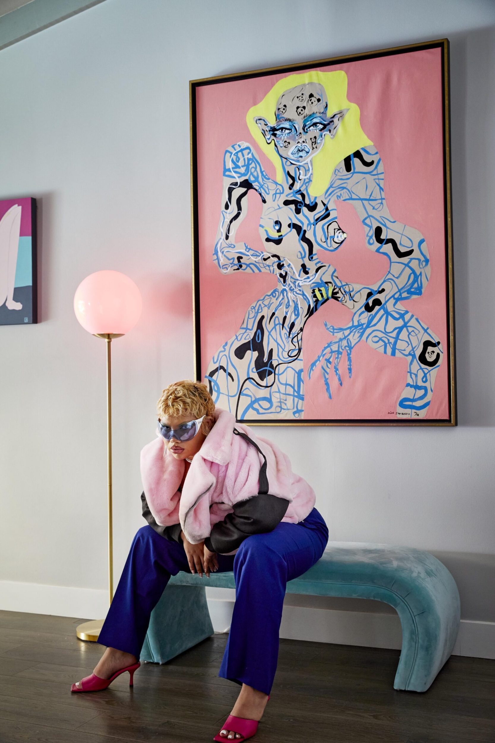 Parris Goebel sitting on a curved blue velvet seat wearing a pink jacket and blue pants