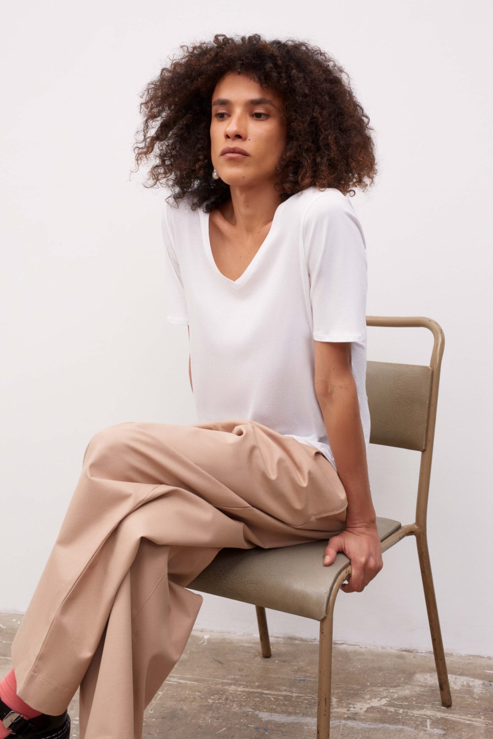 Woman sitting on a chair in a white room wearing a white skirt and beige pants