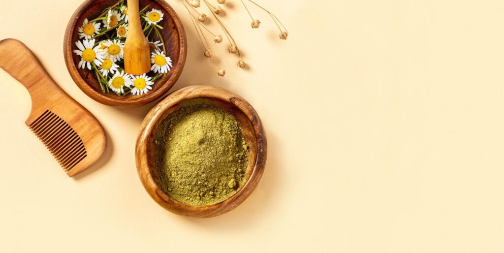 Two brown pots of chamomile flowers and green tea powder against a yellow backdrop