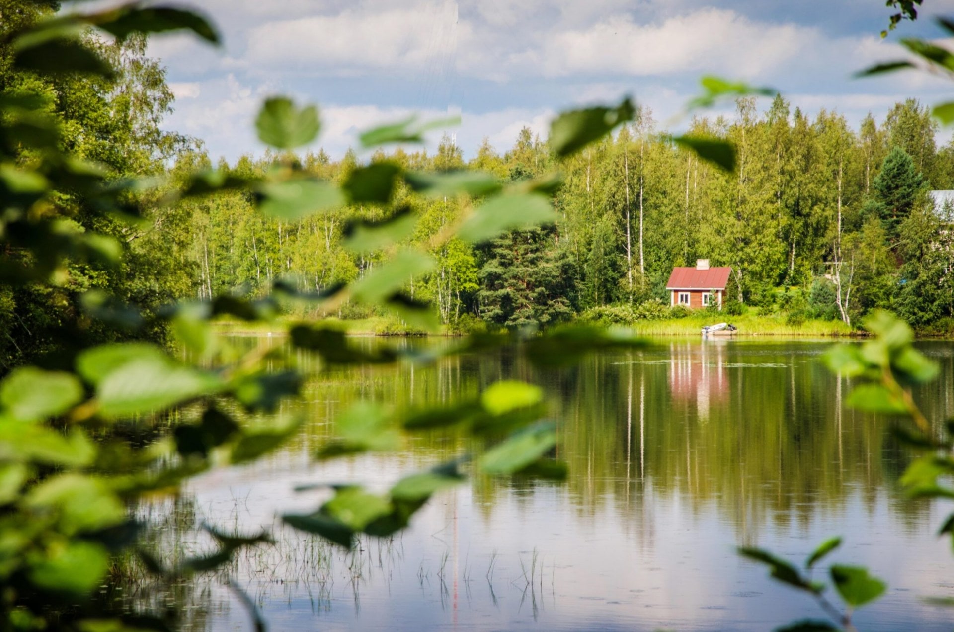 View of a lake seen through leafy trees, with a single red cottage seen on the other side