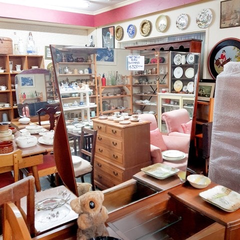 Interior of a vintage store, featuring brown wooden furniture, crockery and mirrors