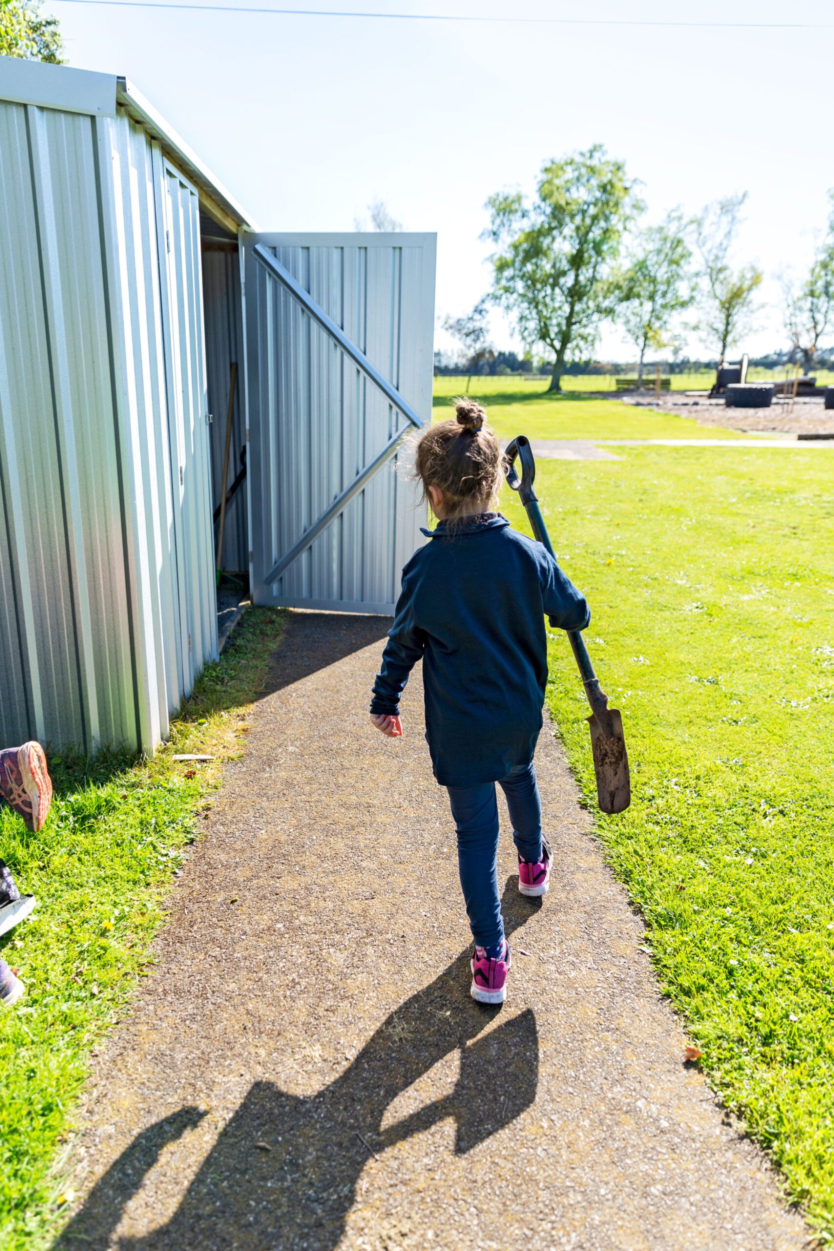 Young girl walking away carrying a spade