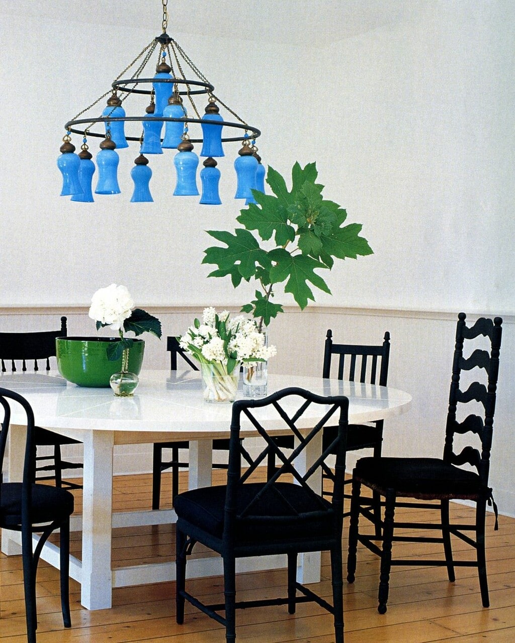 elle decor blue chandelier and black chairs with a white table. 