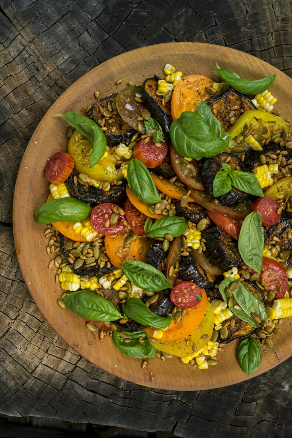 Wooden Bowl with vegetarian Salad in it. Picutred in bowl is tomatoes, basil, corn, eggplant, and seeds.