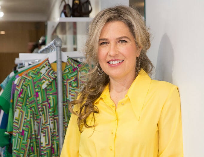 Stylist Stephanie King in a yellow shirt standing in front of rack of clothes