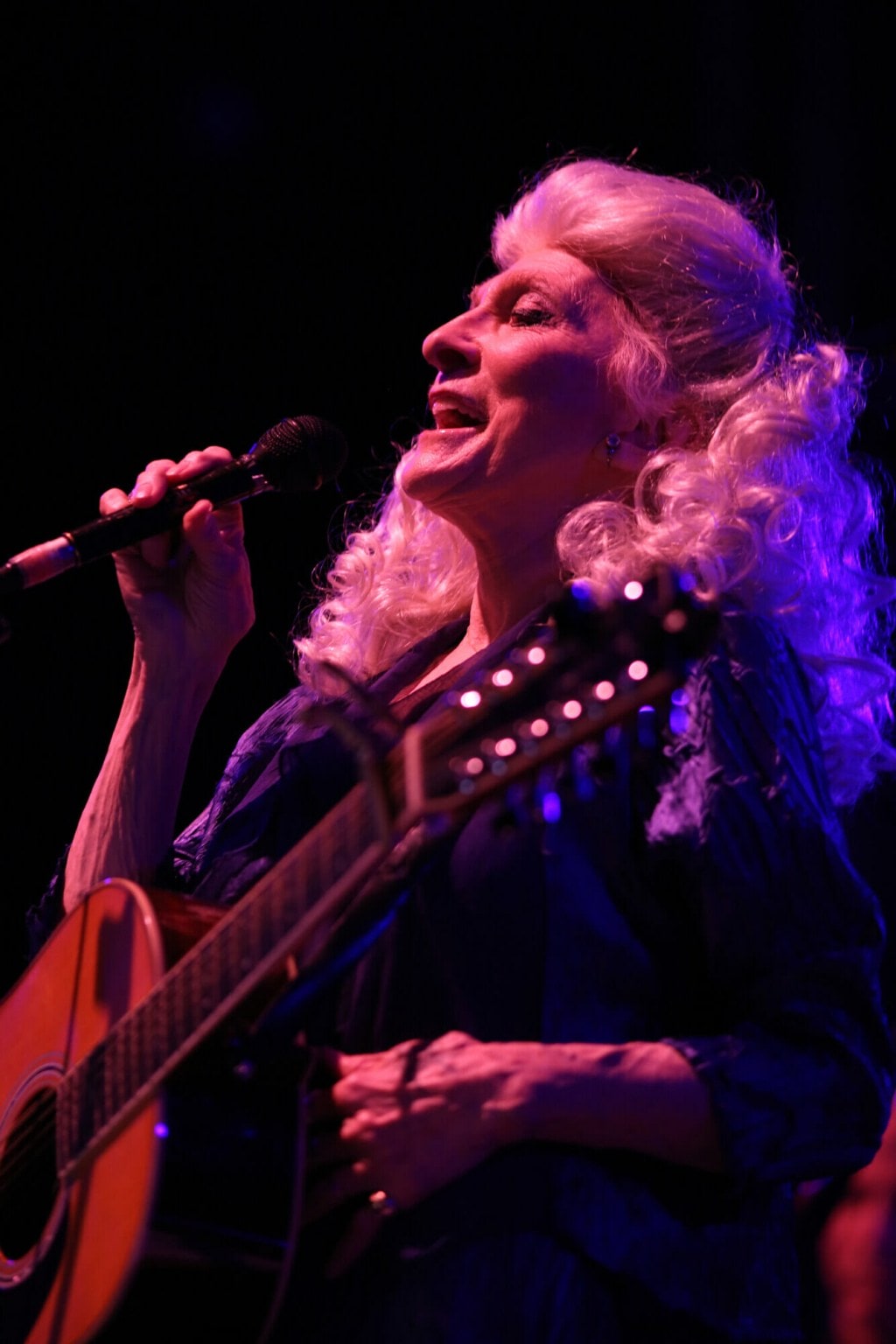 Judy Collins singing into micrphone with guitar