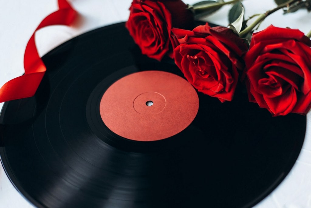 Old black music record, red ribbon and three red roses on white table.