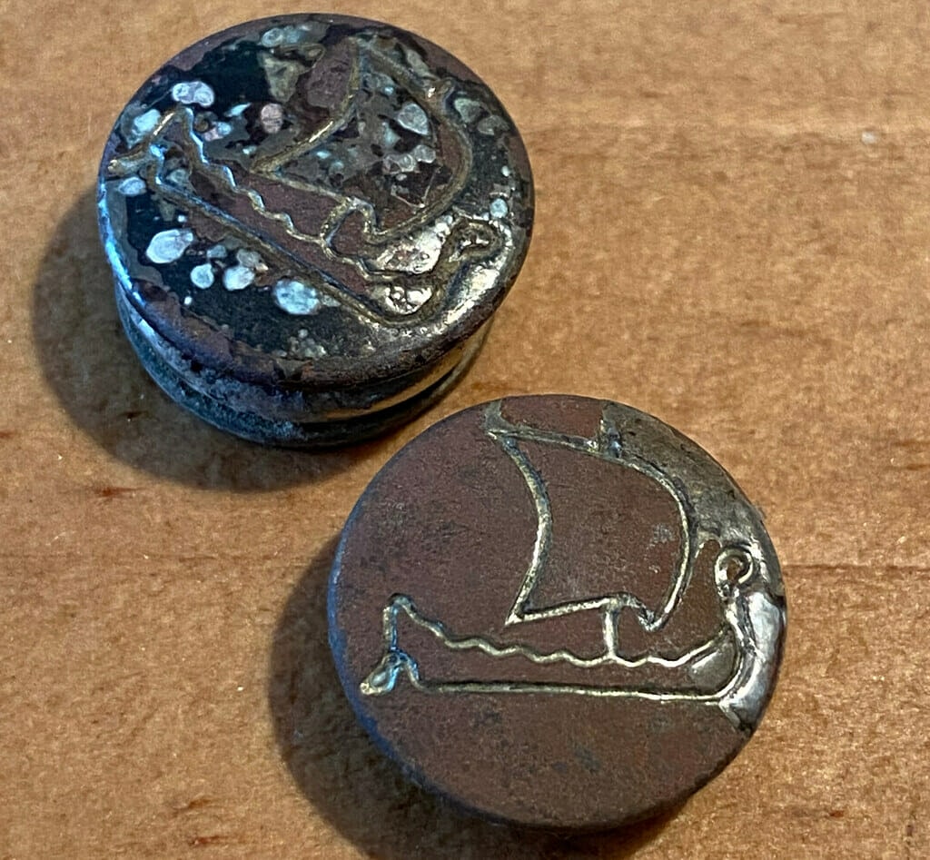 Rusty metal dome buttons with longships engraved on them.
