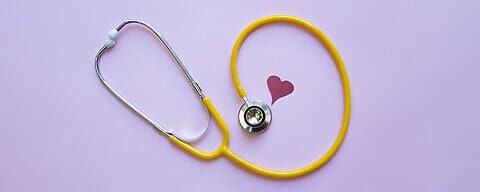 A fun yellow stethoscope on a pink background with a cute cut out heart.