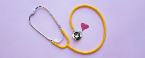 A fun yellow stethoscope on a pink background with a cute cut out heart.