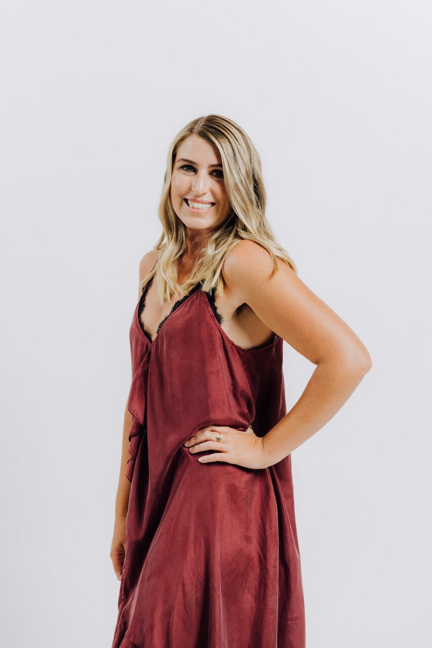 Women standing in front of white background with her hand on her hip. Women is wearing a red silky dress