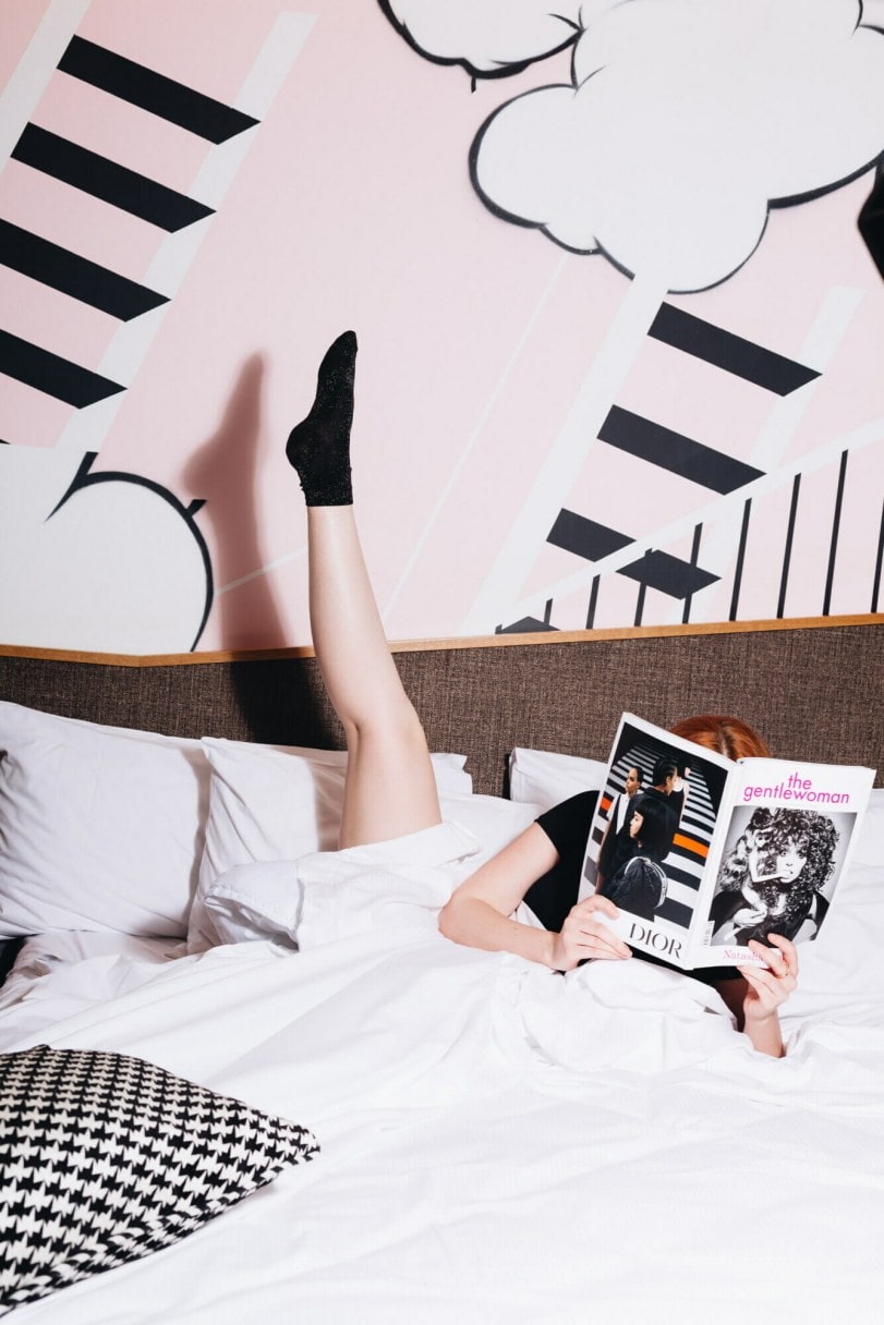 Women laying in bed with leg up and book  'The Gentlewoman' in hand. 