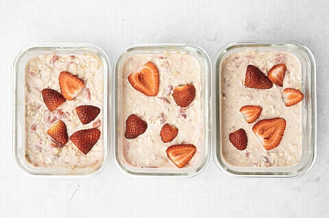 3 containers with pink coloured oats and sliced strawberries on each.