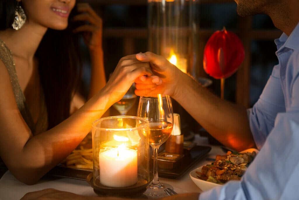 Man and women holding hands in front of candle lit dinner
