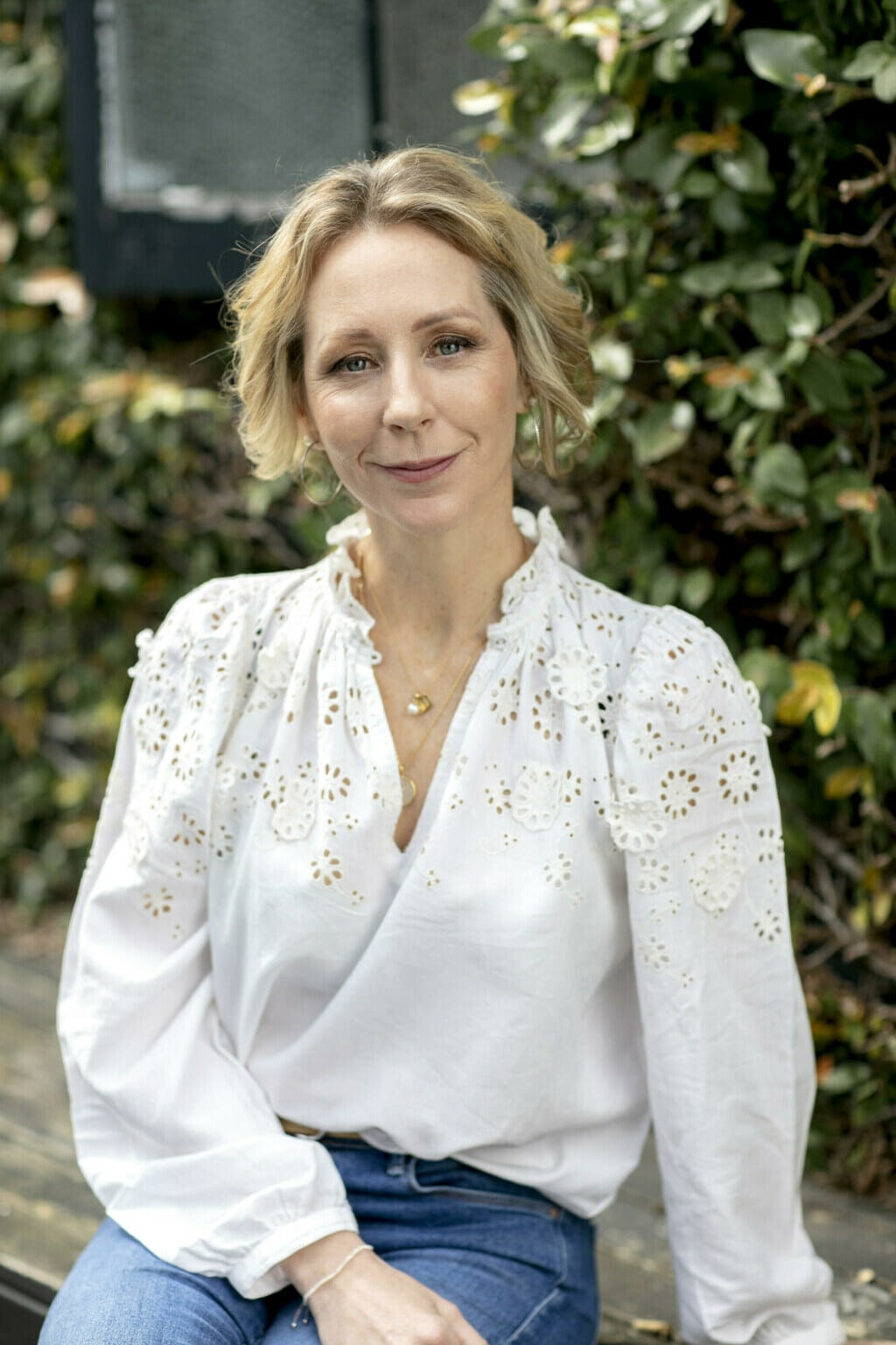 Women in white shirt standing in front of tree. Looking straight on to the camera smiling.