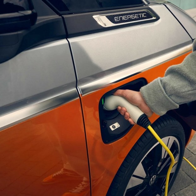 Man plugging charging port into Volkswagen PHEV hybrid van. Orange coloured car. 