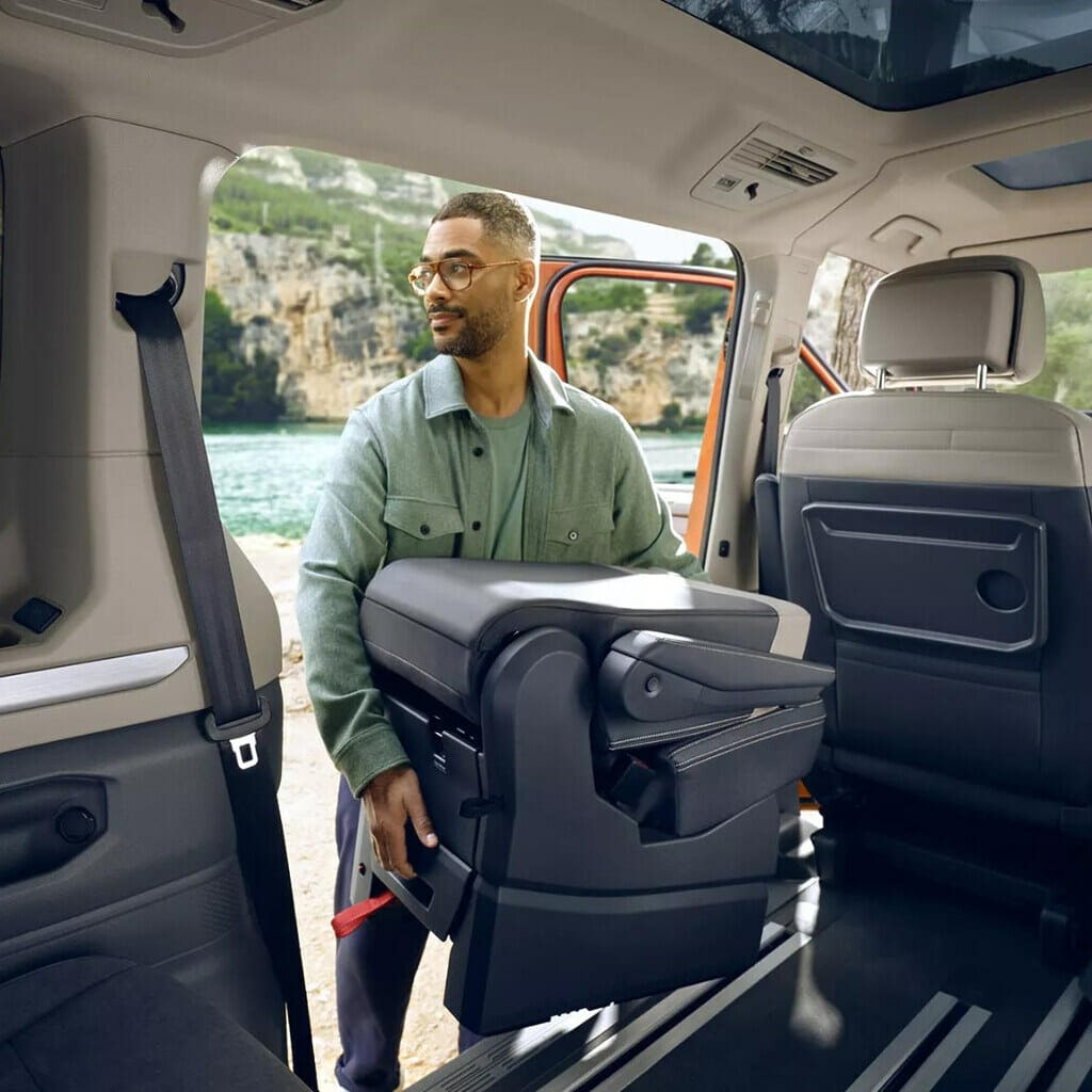 Man in glasses and green shirt lifting removal seat out of PHEV Volkswagen van