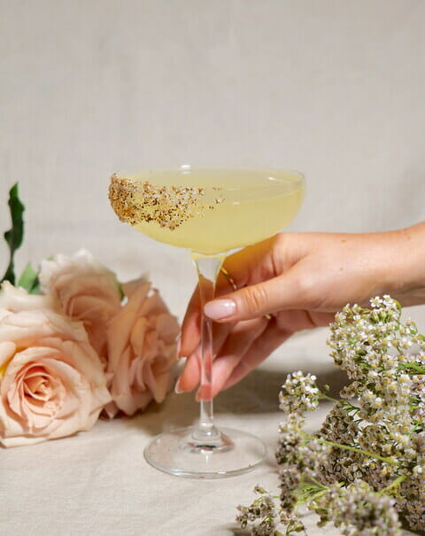manicured hand holding pineapple chilli margarita cocktail with chill salt rim