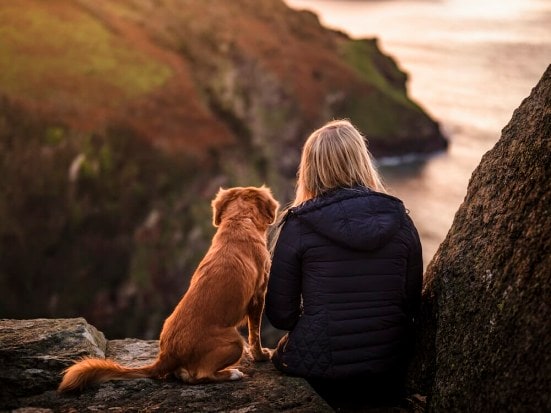 Woman on a cliff watching the sunset with her red haired dog