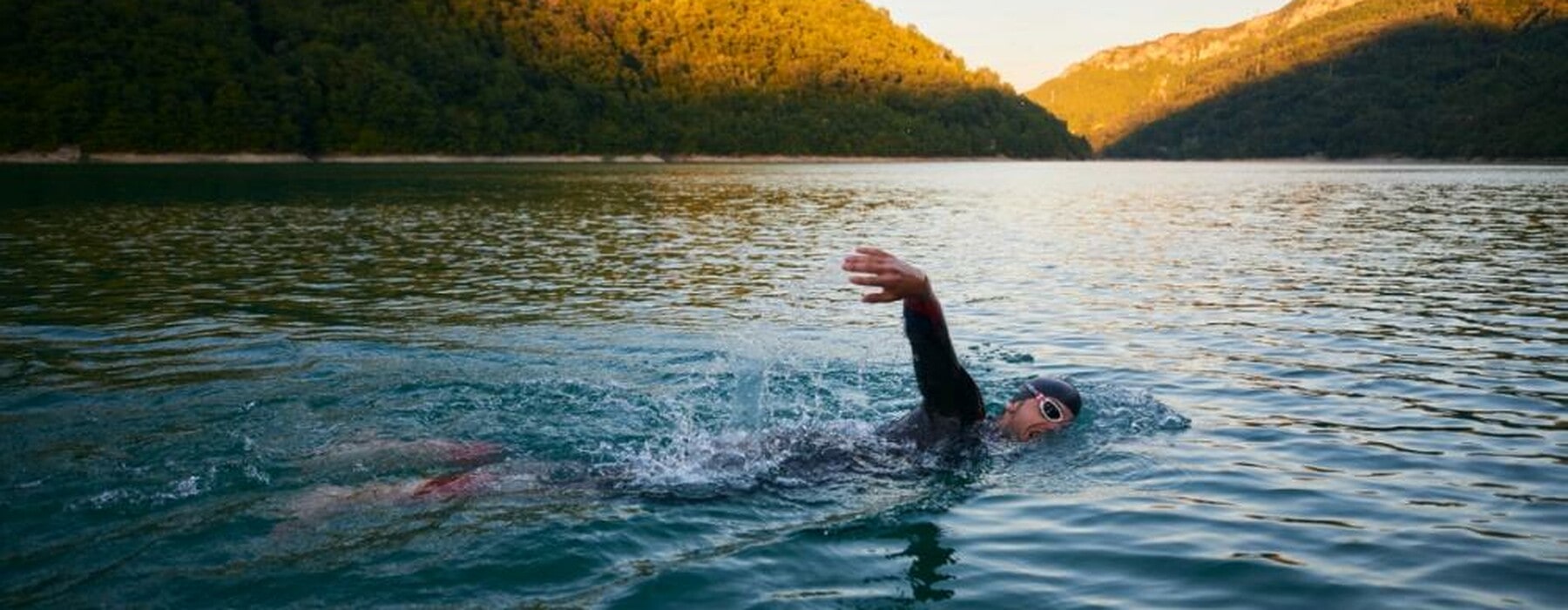 triathlon athlete swimming on lake in sunrise wearing wetsuit