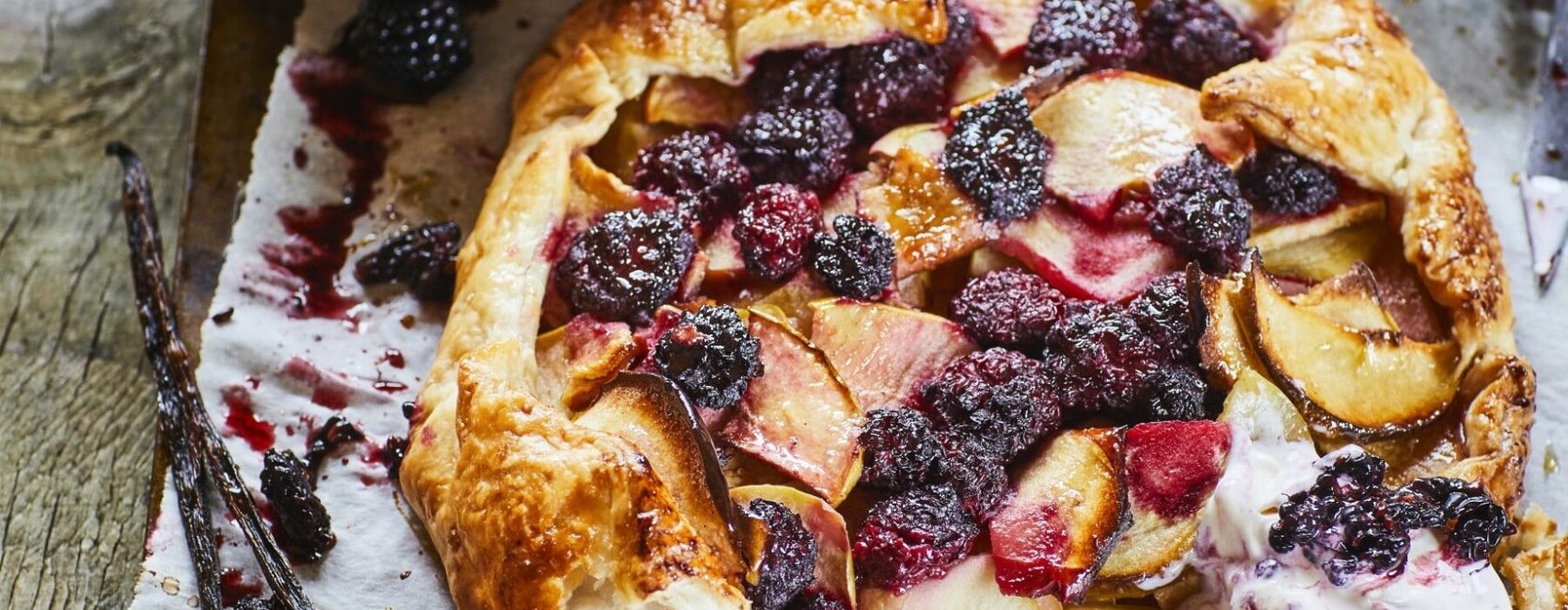 Apple, blackberry and vanilla galette on a silver baking tray next to a bowl of vanilla ice cream