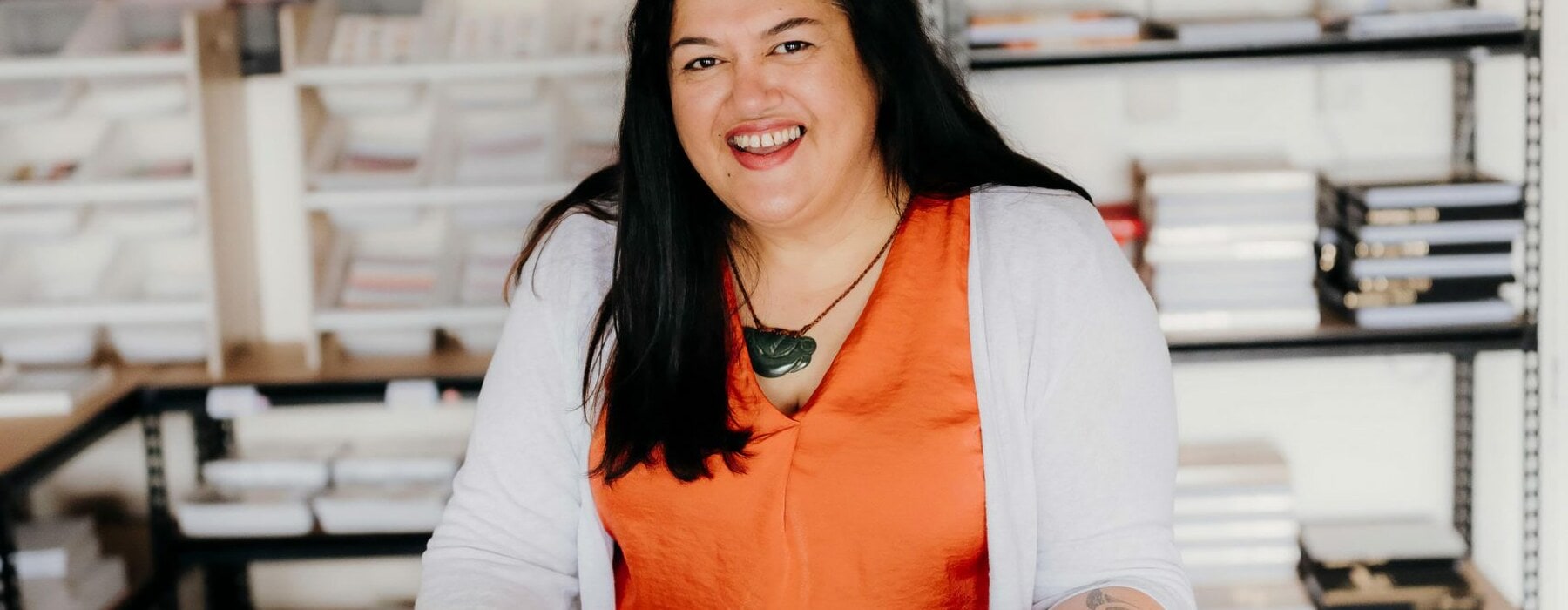 Geneva Harrison holding a Tuhi Stationery planner and wearing an orange top and greenstone necklace