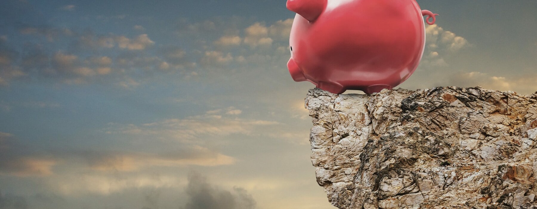 A piggy bank stands at the edge of a cliff and looks over in an image about investment decisions, risk, and challenge.
